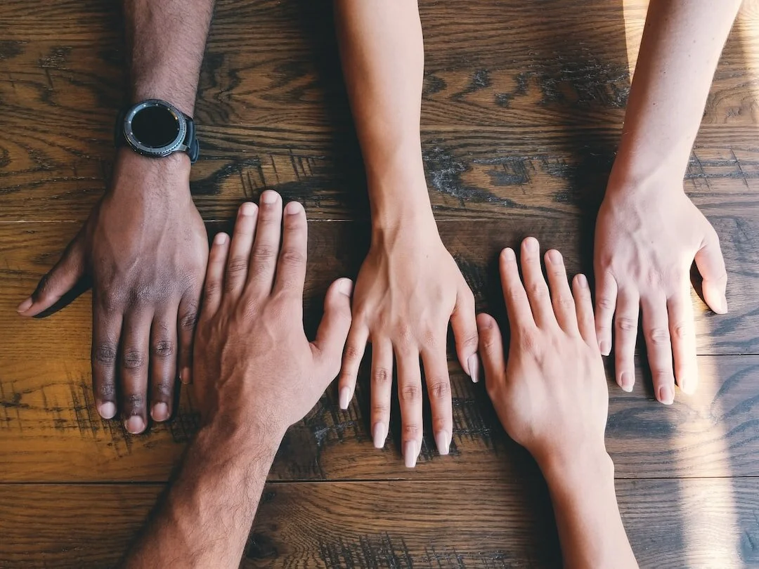 Six hands of different skin tones placed on a wooden table